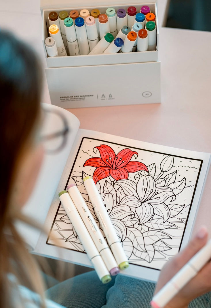 A partly colored lily page in a hand-illustrated coloring book, with alcohol markers alongside
